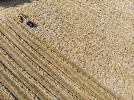 Nature and landscape, aerial view of fields with tractor and harvesting and pressing hay. Field with swaths ready to be transformed into round balesの写真素材