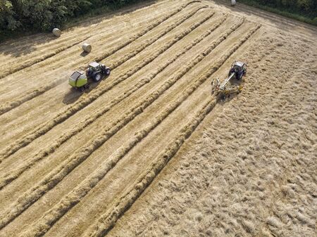 Nature and landscape, aerial view of fields with tractor and harvesting and pressing hay. Field with swaths ready to be transformed into round balesの写真素材