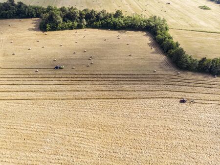 Nature and landscape, aerial view of fields with tractor and harvesting and pressing hay. Field with swaths ready to be transformed into round balesの写真素材