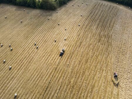 Nature and landscape, aerial view of fields with tractor and harvesting and pressing hay. Field with swaths ready to be transformed into round balesの写真素材