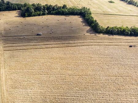 Nature and landscape, aerial view of fields with tractor and harvesting and pressing hay. Field with swaths ready to be transformed into round balesの写真素材