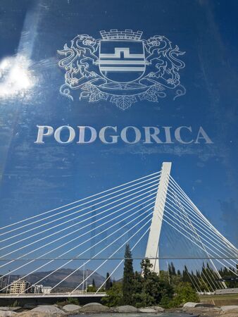 Podgorica, emblem of the capital printed on a transparent panel on the Moscow Bridge. In the background the Millenium bridge. 09/15/2019. Modern architecture of the capital of Montenegroの写真素材