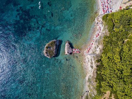 Aerial view of Sveti Nikola, Budva island, Montenegro. Hawaii beach, umbrellas and bathers and crystal clear waters. Jagged coasts with sheer cliffs overlooking the transparent sea. Wild nature and Mediterranean maquisの写真素材
