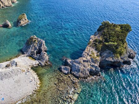 Aerial view of Sveti Nikola, Budva island, Montenegro. Hawaii beach, umbrellas and bathers and crystal clear waters. Jagged coasts with sheer cliffs overlooking the transparent sea. Wild nature and Mediterranean maquisの写真素材