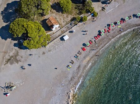 Aerial view of Sveti Nikola, Budva island, Montenegro. Hawaii beach, umbrellas and bathers and crystal clear waters. Jagged coasts with sheer cliffs overlooking the transparent sea. Wild nature and Mediterranean maquisの写真素材