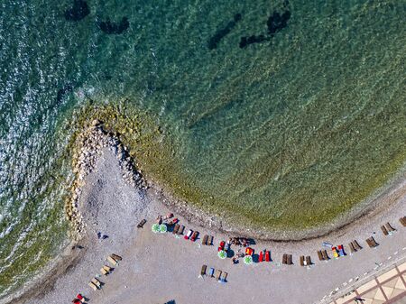 Aerial view of Sveti Nikola, Budva island, Montenegro. Hawaii beach, umbrellas and bathers and crystal clear waters. Jagged coasts with sheer cliffs overlooking the transparent sea. Wild nature and Mediterranean maquisの写真素材