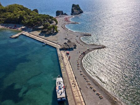 Aerial view of Sveti Nikola, Budva island, Montenegro. Hawaii beach, umbrellas and bathers and crystal clear waters. Jagged coasts with sheer cliffs overlooking the transparent sea. Wild nature and Mediterranean maquisの写真素材