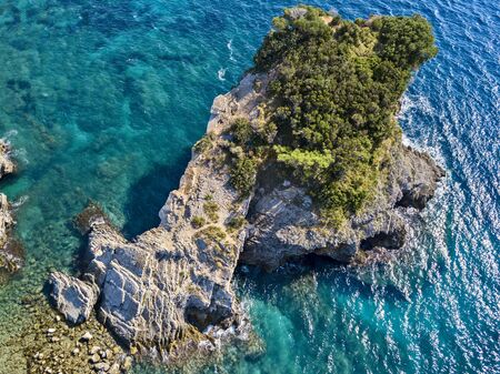 Aerial view of Sveti Nikola, Budva island, Montenegro. Hawaii beach, umbrellas and bathers and crystal clear waters. Jagged coasts with sheer cliffs overlooking the transparent sea. Wild nature and Mediterranean maquisの写真素材