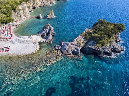 Aerial view of Sveti Nikola, Budva island, Montenegro. Hawaii beach, umbrellas and bathers and crystal clear waters. Jagged coasts with sheer cliffs overlooking the transparent sea. Wild nature and Mediterranean maquisの写真素材
