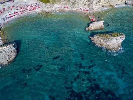 Aerial view of Sveti Nikola, Budva island, Montenegro. Hawaii beach, umbrellas and bathers and crystal clear waters. Jagged coasts with sheer cliffs overlooking the transparent sea. Wild nature and Mediterranean maquisの写真素材