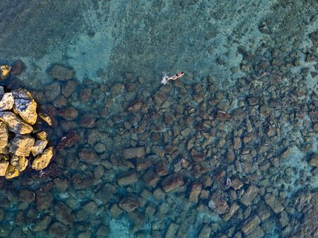 Aerial view of rocks on the sea. Overview of seabed seen from above, transparent water. Swimmers,...