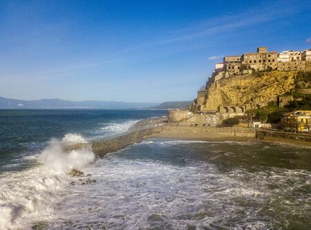 Aerial view of Pizzo Calabro, broken pier, castle, Calabria, tourism Italy. Houses on the rock. On the cliff stands the Murat Aragonese castle. Seafront at sunset. Sea storm and waves with windの写真素材
