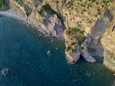 Aerial view of a steep cliff and a motor boat. Jagged coast on the Adriatic Sea. Cliffs overlooking the transparent sea. Wild nature and Mediterranean maquisの写真素材