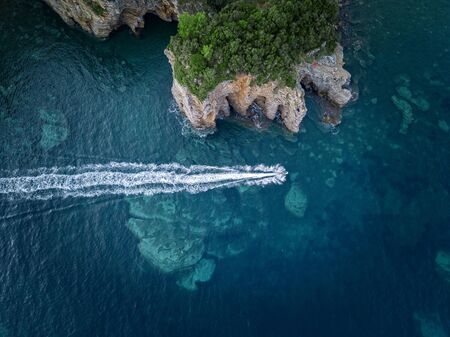 Aerial view of a steep cliff and a motor boat. Jagged coast on the Adriatic Sea. Cliffs overlooking the transparent sea. Wild nature and Mediterranean maquisの写真素材