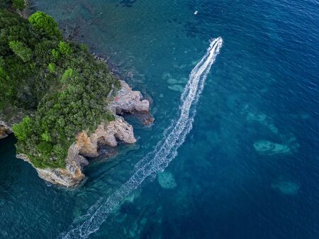 Aerial view of a steep cliff and a motor boat. Jagged coast on the Adriatic Sea. Cliffs overlooking the transparent sea. Wild nature and Mediterranean maquisの写真素材