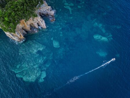 Aerial view of a steep cliff and a motor boat. Jagged coast on the Adriatic Sea. Cliffs overlooking the transparent sea. Wild nature and Mediterranean maquisの写真素材