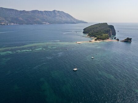 Aerial view of a boat near the island of Sveti Nikola, island of Budva, Montenegro. Jagged coasts with sheer cliffs overlooking the transparent sea. Wild nature and Mediterranean maquisの写真素材