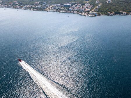 Aerial view of a red motor boat speeds by in the Kotor fjord in Montenegro. Mediterranean maquis vegetation and unspoiled natureの写真素材
