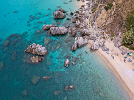 Aerial view of a beach and umbrellas. Tropea, Calabria, Italy. Parghelia. Overview of seabed seen from above, transparent water. Swimmers, bathers floating on the water. Beach and rocks of Vardanelloの写真素材
