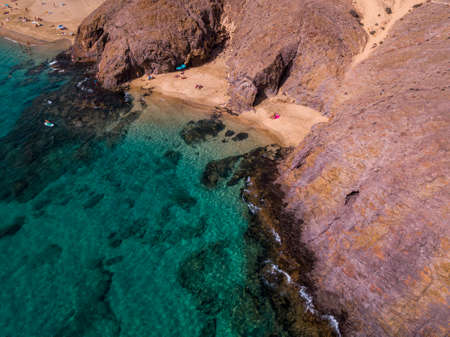 Aerial view of the jagged shores and beaches of Lanzarote, Spain, Canary. Roads and dirt paths. Walking routes to explore the island. Bathers on the beach. Atlantic Ocean. Papagayoの写真素材