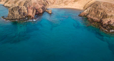 Aerial view of the jagged shores and beaches of Lanzarote, Spain, Canary. Roads and dirt paths. Walking routes to explore the island. Bathers on the beach. Atlantic Ocean. Papagayoの写真素材