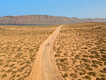 Aerial view of people cycling on a dirt path in the island of La Graciosa, Lanzarote, Canary Islands. Spain. In the background El risco, the mountainous part to the north of Lanzaroteの写真素材