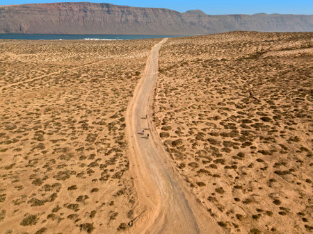 Aerial view of people cycling on a dirt path in the island of La Graciosa, Lanzarote, Canary Islands. Spain. In the background El risco, the mountainous part to the north of Lanzaroteの写真素材