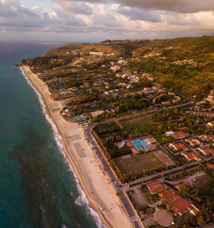 Aerial view of a sunset over the sea in Zambrone, coast of Calabria. Italy. Houses and trees near the beach with umbrellas. Tourist resorts and holidaysの写真素材
