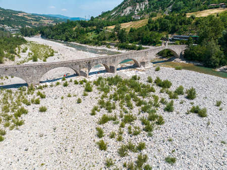Aerial view. Drought and dry rivers. Roman bridge of Bobbio over the Trebbia river, Piacenza, Emilia-Romagna. Italy. River bed with stones and vegetation. Called hunchback bridgeの写真素材