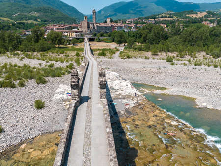 Aerial view. Drought and dry rivers. Roman bridge of Bobbio over the Trebbia river, Piacenza, Emilia-Romagna. Italy. River bed with stones and vegetation. Called hunchback bridgeの写真素材
