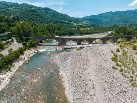 Aerial view. Drought and dry rivers. Roman bridge of Bobbio over the Trebbia river, Piacenza, Emilia-Romagna. Italy.River bed with stones and vegetation. Called hunchback bridgeの写真素材