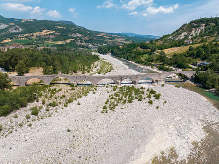 Aerial view. Drought and dry rivers. Roman bridge of Bobbio over the Trebbia river, Piacenza, Emilia-Romagna. Italy. River bed with stones and vegetation. Called hunchback bridgeの写真素材