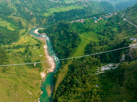 Aerial view of a Tibetan suspended bridge in Nepal is a primitive type of bridge in which the deck lies on two parallel load-bearing cables that are anchored at either endの写真素材