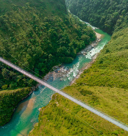 Aerial view of a Tibetan suspended bridge in Nepal is a primitive type of bridge in which the deck lies on two parallel load-bearing cables that are anchored at either endの写真素材