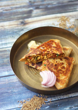 Stuffed Indian Egg paratha. A stuffed bread(paratha) cut into two pieces and served on a traditional plate with ghee/ butter and onion on the side.の写真素材