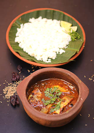 Kerela traditional fish curry and rice served in terracotta utensil on black background.の写真素材
