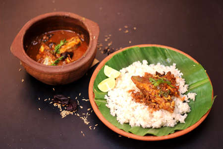 Kerela traditional fish curry and rice served in terracotta utensil on black background.の写真素材