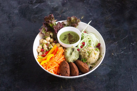 Lebanese Falafel bowl with chickpeas, cucumber, peppers, and carrots in a white bowl. stylized in a large bowl on a rustic black backgroundの写真素材