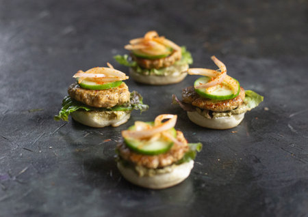 Open chicken sliders with moist juicy chicken patty, onions, mayo, and pickled onion on the side on a black backgroundの写真素材