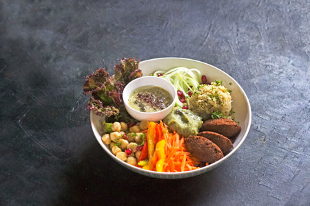Lebanese Falafel bowl with chickpeas, cucumber, peppers, and carrots in a white bowl. stylised in a white large bowl on rustic black backgroundの写真素材