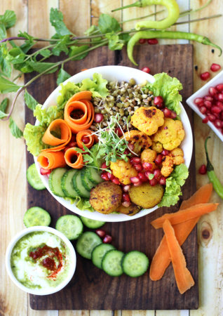 Indian Sprouts rainbow salad with fresh vegetables and curled-up carrots, sweet potato, and mint yogurt chutney on the side. Stylised on a rustic wooden plankの写真素材