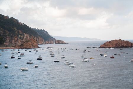 Island formed of rocks in the middle of the sea surrounded by boatsの写真素材