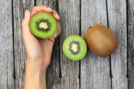 Hand holding half kiwi fruits on wooden table backgroundの写真素材
