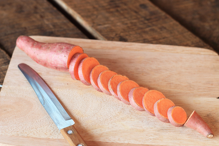 Raw sweet potatoes on a kitchen cutting boardの写真素材