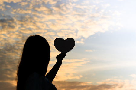 Silhouette of women hands holding heart shape at the sky sunset background.の写真素材