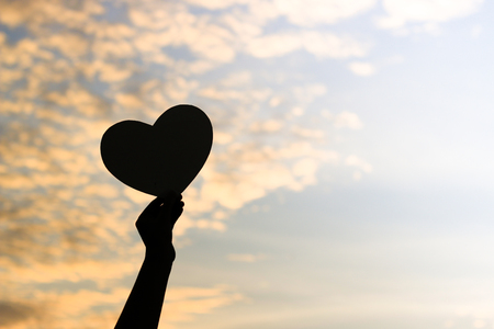 Silhouette of women hands holding heart shape at the sky sunset background.の写真素材