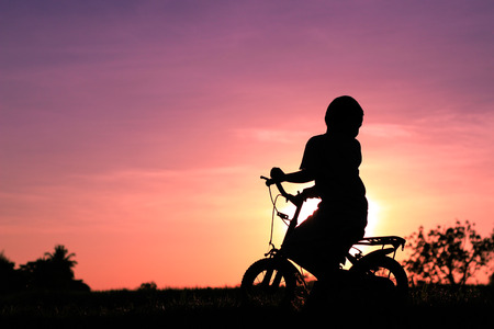 little boy riding bike at sunsetの写真素材