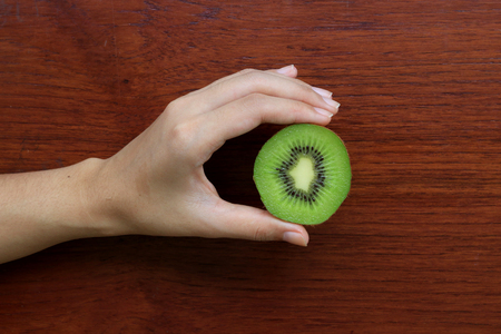 Hand holding half kiwi fruits on wooden table backgroundの写真素材