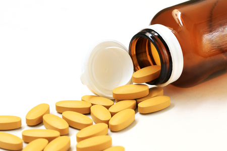 Pills of vitamin C spilled out open bottle on white background.