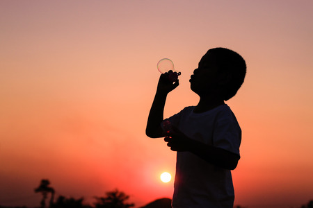 Cute little boy is blowing a soap bubbles at summer sunsetの写真素材
